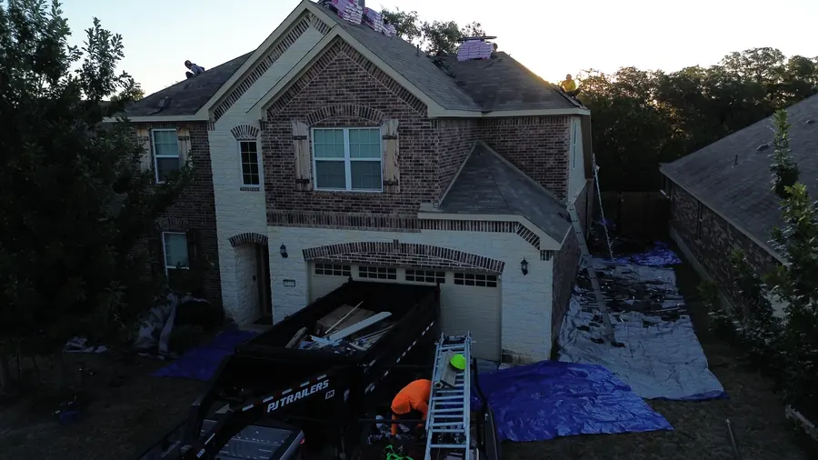 Dump trailer and ground tarps set up in front of a San Antonio home during a roof replacement
